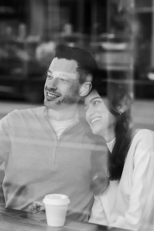 Couple sharing a quiet, cinematic moment inside an Ottawa coffee shop, captured through the window during an at-home style portrait session