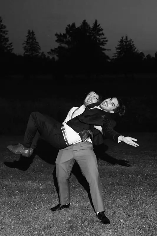 A group of groomsmen joyfully lifting the groom into the air during a night-time wedding celebration with professional flash photography.