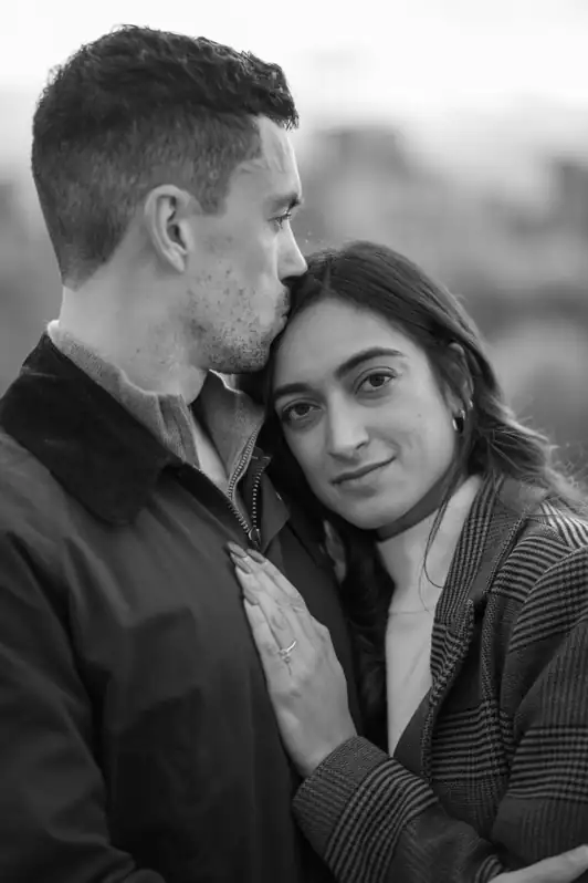 A close-up, intimate portrait of a fiancée resting her head on her partner's chest while he gently kisses her forehead during an engagement session.