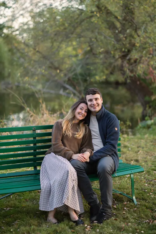 A couple sitting intimately on a rustic park bench overlooking the tranquil pond at the historic Dominion Arboretum in Ottawa, Ontario.