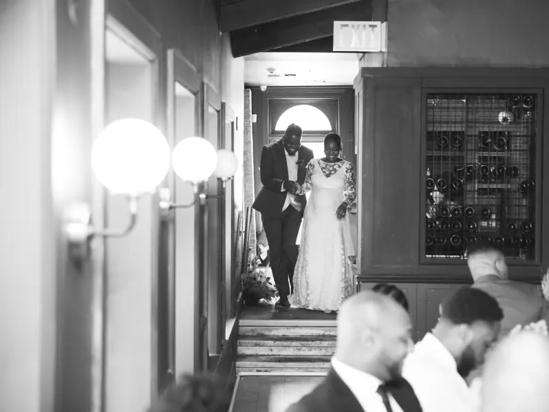 A bride and groom walking down a grand staircase into their wedding reception, cheering and celebrating as their guests applaud.