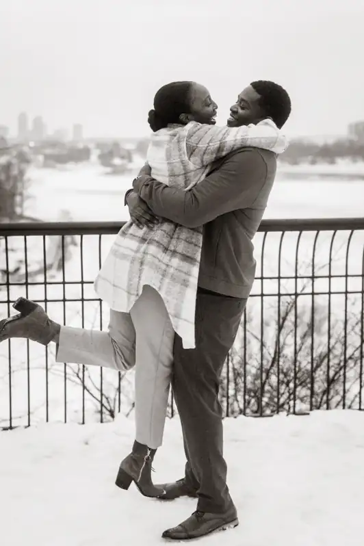 A wife jumping joyfully into her husband's arms during a winter anniversary session in a snow-covered Ottawa park, both laughing.